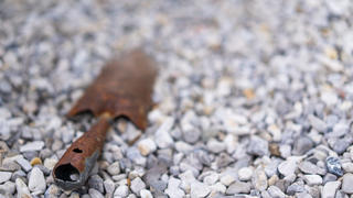 rusty garden shovel in gravel with place for text, shallow focus on foreground, background blurred