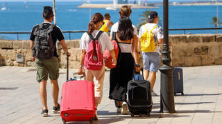 26.07.2020, Spanien, Palma: Menschen gehen mit ihren Rollkoffern durch die Stadt. Urlauber, die aus dem Ausland nach Deutschland zurückkehren, können sich nach ihrer Rückkehr kostenlos auf das Virus testen lassen. Foto: Clara Margais/dpa +++ dpa-Bildfunk +++