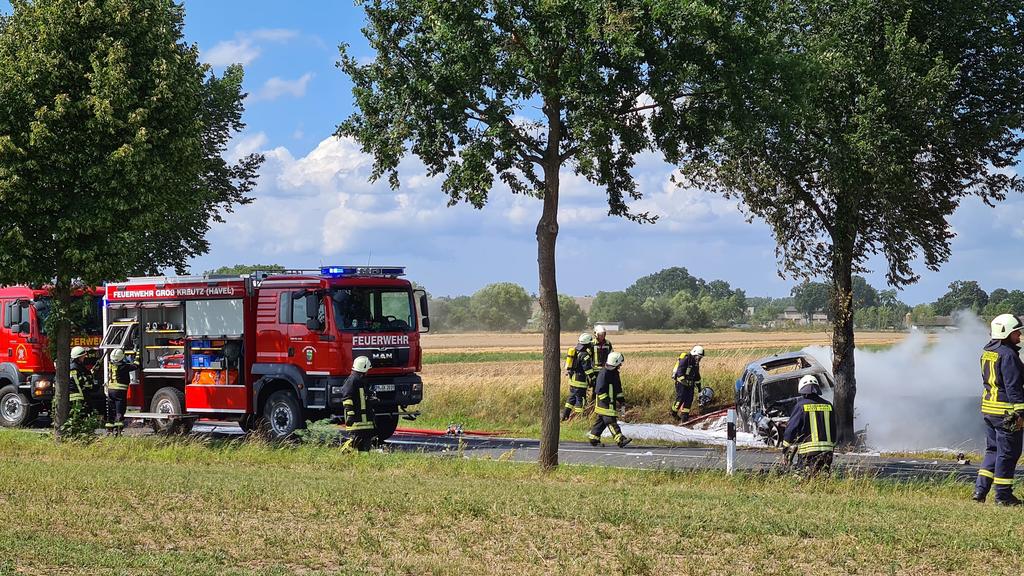 28.07.2020, Brandenburg, Groß Kreutz: Feuerwehrleute löschen das Unfallwrack eines Autos. Eine junge Fahrerin ist in Groß Kreutz bei Potsdam mit dem Auto gegen einen Baum geprallt und darin verbrannt. Es sei schwierig gewesen, die Frau in dem Elektro
