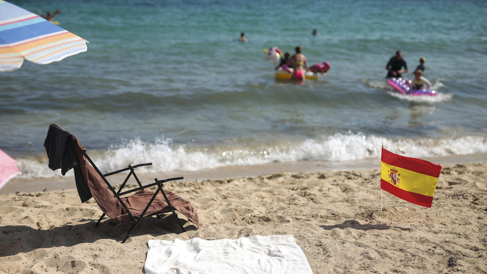 26.07.2020, Spanien, Mallorca: Eine spanische Flagge, die als soziale Distanzierungsbeschilderung verwendet wird, ragt am Strand in Palma de Mallorca Sand hervor. Spanien verhandelt mit Großbritannien darüber, die Balearen und die Kanaren von der sei