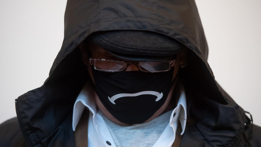 Der Angeklagte verbirgt sein Gesicht hinter einer Gesichtsmaske, einer Brille und unter einer Kapuze.