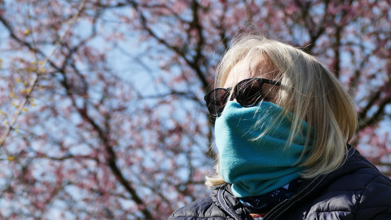 Frau hat eine Sonnenbrille auf und trägt einen Schal vor dem Mund