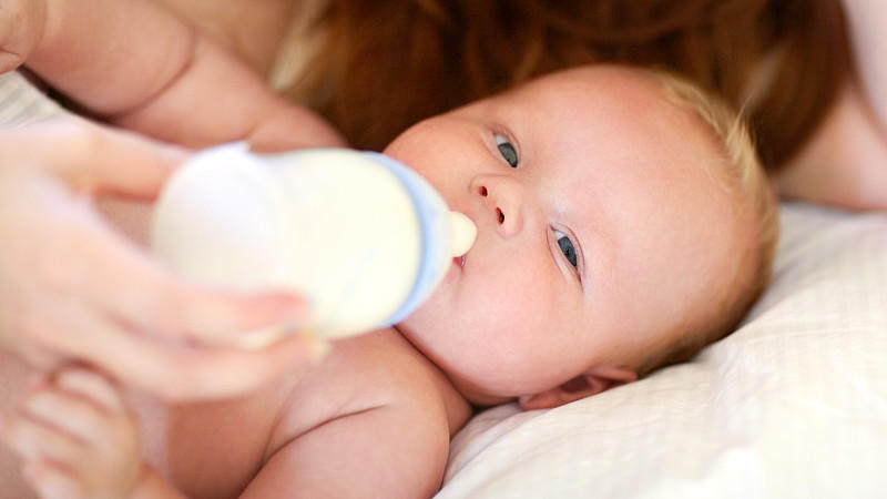 Sorgende Mutter versucht ihr Baby zu füttern mit einer Milchflasche