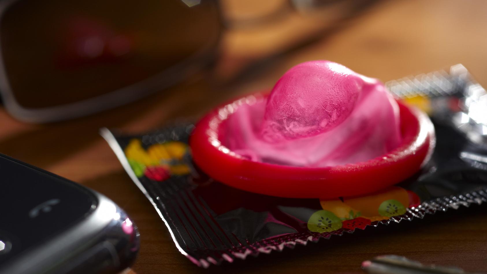 Ein Kondom liegt auf einem Tisch neben einem Handy, einem Autoschlüssel und einer Sonnenbrille, Symbolbild Untreue | Verwendung weltweit, Keine Weitergabe an Wiederverkäufer.