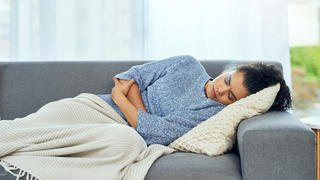 Frau liegt mit Menstruationsschmerzen auf dem Sofa.