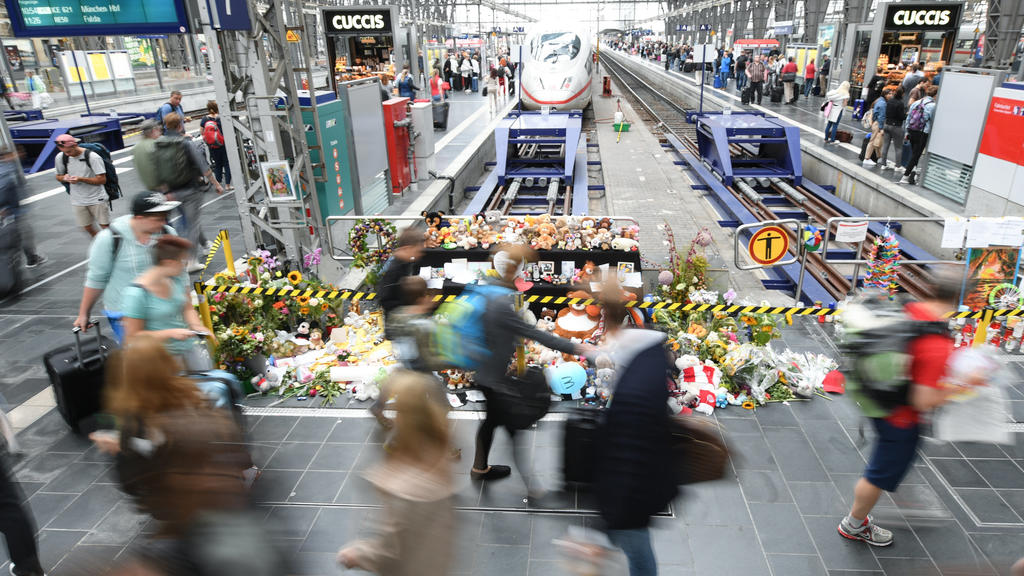 ARCHIV - 20.08.2019, Hessen, Frankfurt/Main: Passanten gehen am Gleis 7 des Hauptbahnhofs an einer Gedenkstelle vorbei, an der sich Blumen, Kuscheltiere und Beileidsbekundungen angesammelt haben (Aufnahme mit längerer Verschlusszeit). Am 29. Juli 201