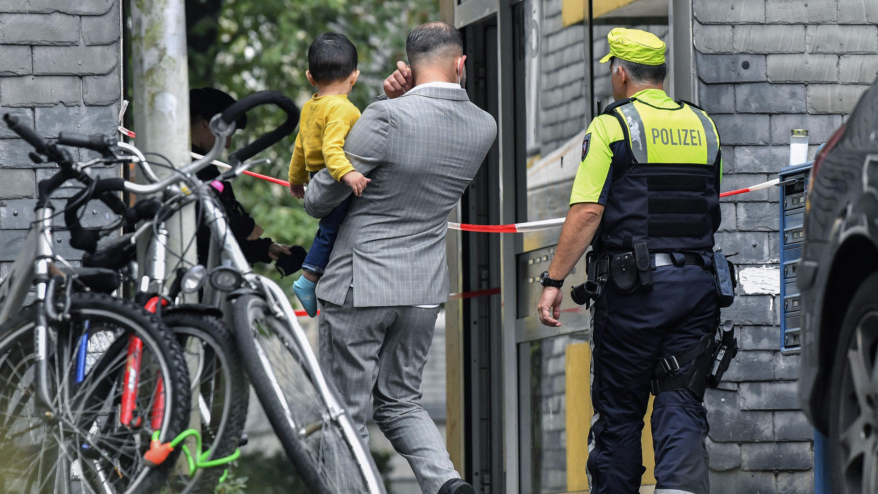 Residents enter a house with a police officer, where five dead children were found in Solingen, Germany, Thursday, Sept. 3, 2020. Police say the five children have been found dead at an apartment in the western German city, and their mother is suspec