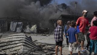 Fire burns container houses as children stand next to the burned debris in the Moria refugee camp on the northeastern Aegean island of Lesbos, Greece, on Wednesday, Sept. 9, 2020. A major overnight fire swept through Greece's largest refugee camp, that had been placed under COVID-19 lockdown, leaving more than 12,000 migrants in emergency need of shelter on the island of Lesbos. (AP Photo/Petros Giannakouris)