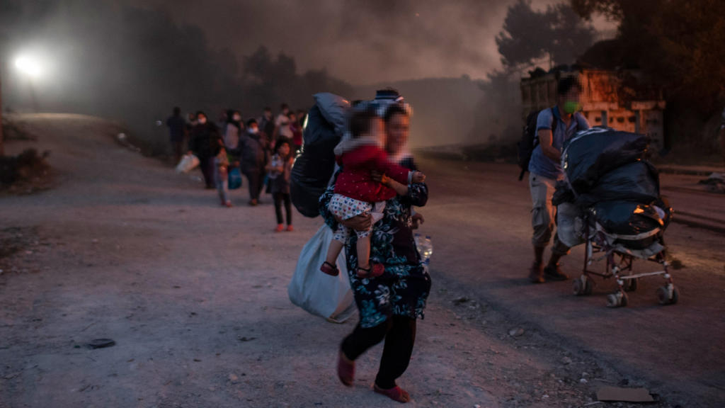 09.09.2020, Griechenland, Lesbos: Migranten fliehen vor einem erneuten Feuers mit ihren Habseligkeiten aus dem Flüchtlingslager Moria, nachdem zuvor bereits mehrere Feuer das Lager nahezu vollständig zerstört haben. Vorangegangen waren Unruhen unter 