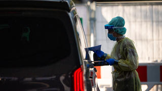 13.09.2020, Bayern, Garmisch-Partenkirchen: Eine Mitarbeiterin gibt in einem Testzentrum einer Familie in einem Auto Infomaterial zum Coronavirus. Nach einem heftigen Corona-Ausbruch im oberbayerischen Garmisch-Partenkirchen ist noch unklar, mit welchen Konsequenzen die mutmaßliche Verursacherin rechnen muss. Die Behörde geht davon aus, dass der Ausbruch auf eine sogenannte Superspreaderin zurückzuführen ist. Foto: Lino Mirgeler/dpa +++ dpa-Bildfunk +++