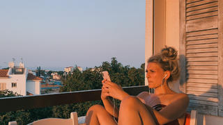 Frau sitzt auf Balkon im roten Abendlicht