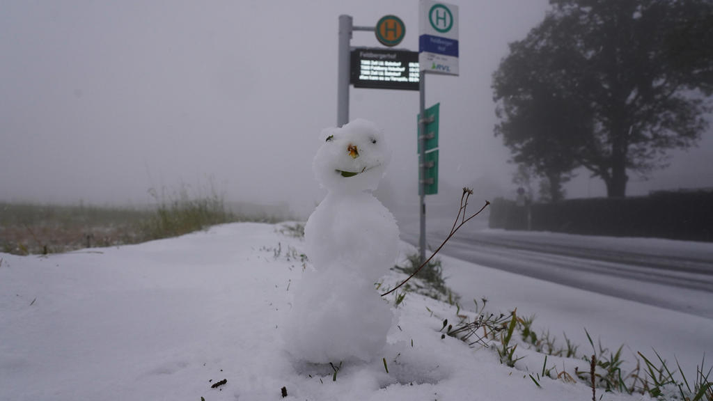 Ein kleiner Schneemann steht neben einer Bushaltestelle neben einer weiß verschneiten Straße auf dem Feldberg im Schwarzwald.