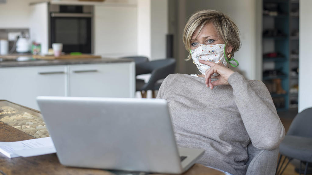 Frau mit Mundschutz arbeitet am laptop *** Woman with mouth guard working on laptop