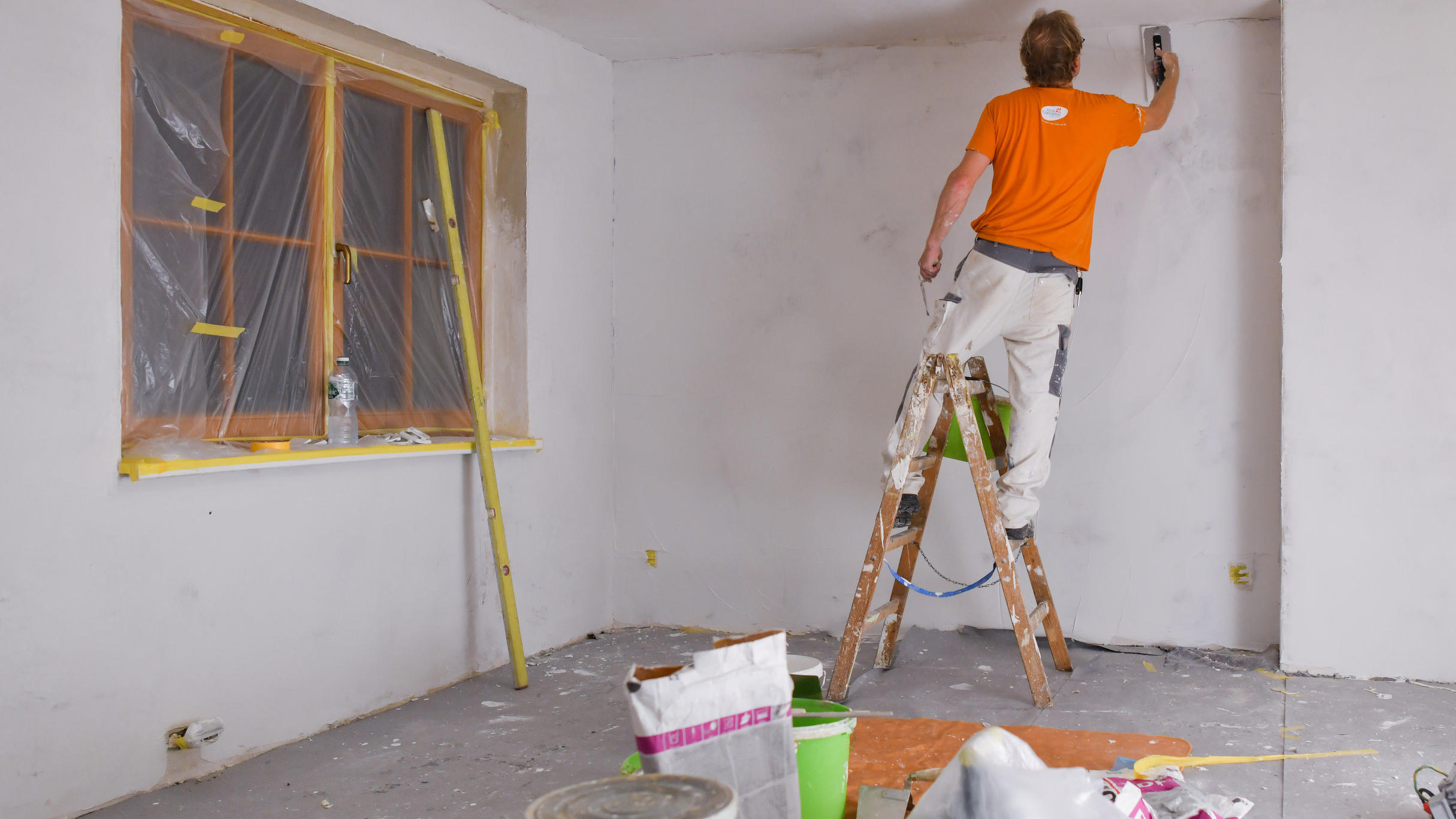 Ein Maler spachtelt die Wände eines Zimmers glatt.