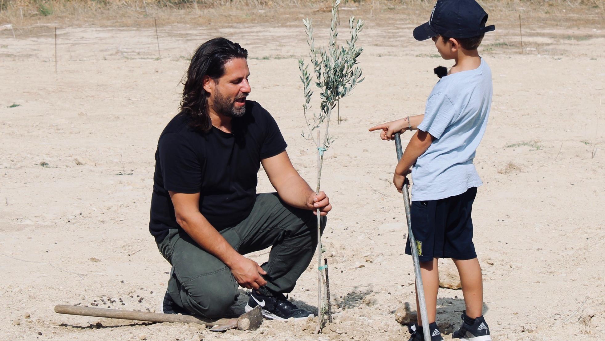 Adam Bousdoukos und kleiner Junge knien vor junger Pflanze