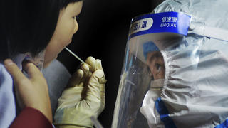 15.10.2020, China, Qingdao: Ein medizinisches Personal im Schutzanzug nimmt einen Abstrich von einem Kind in der Nähe eines Wohngebiets. Nach einem neuen Ausbruch des Coronavirus hat die ostchinesische Metropole Qingdao innerhalb von vier Tagen einen Massentest bei zehn Millionen Menschen durchgeführt. Foto: CHINATOPIX/AP/dpa +++ dpa-Bildfunk +++