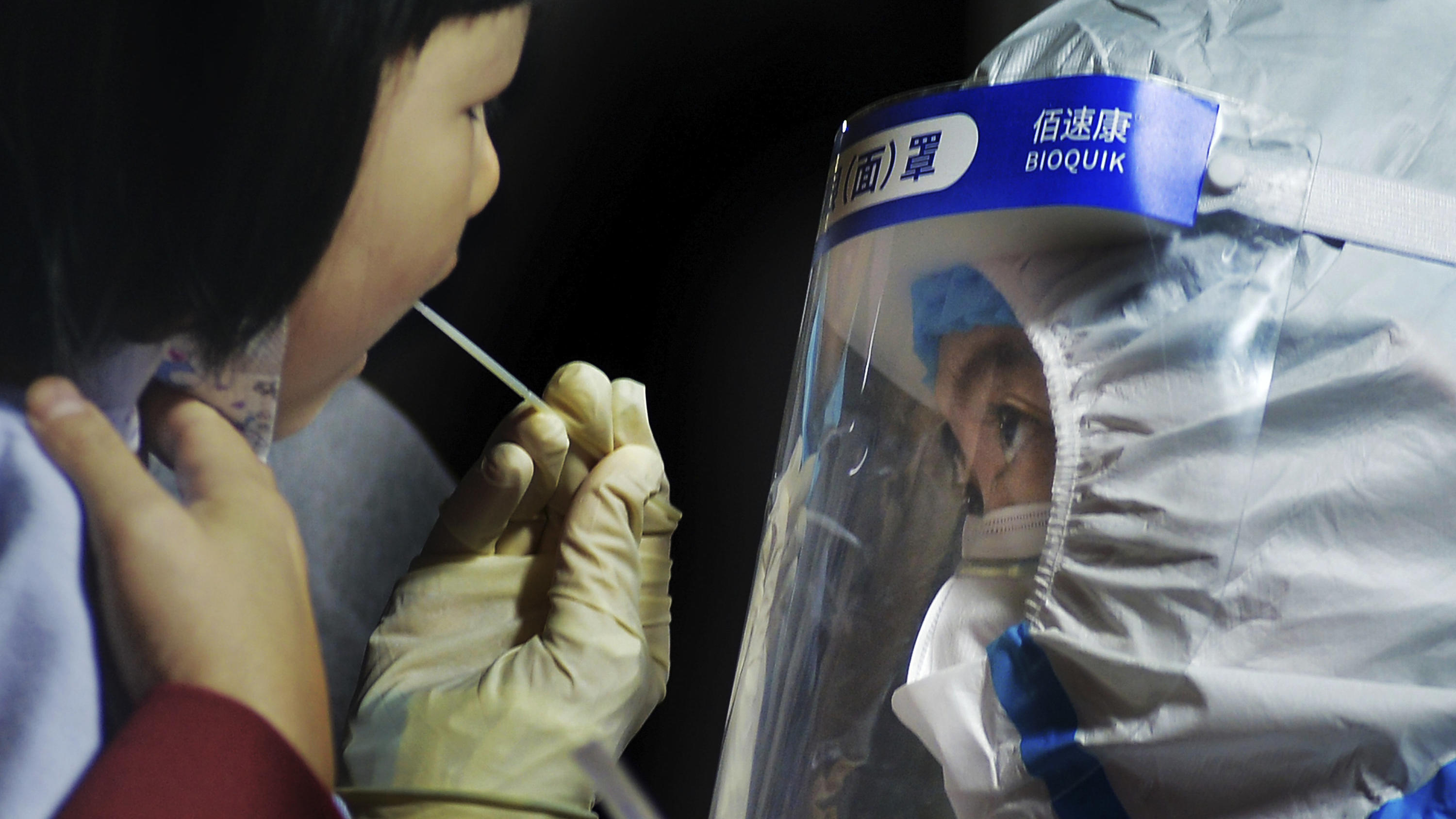 15.10.2020, China, Qingdao: Ein medizinisches Personal im Schutzanzug nimmt einen Abstrich von einem Kind in der Nähe eines Wohngebiets. Nach einem neuen Ausbruch des Coronavirus hat die ostchinesische Metropole Qingdao innerhalb von vier Tagen einen