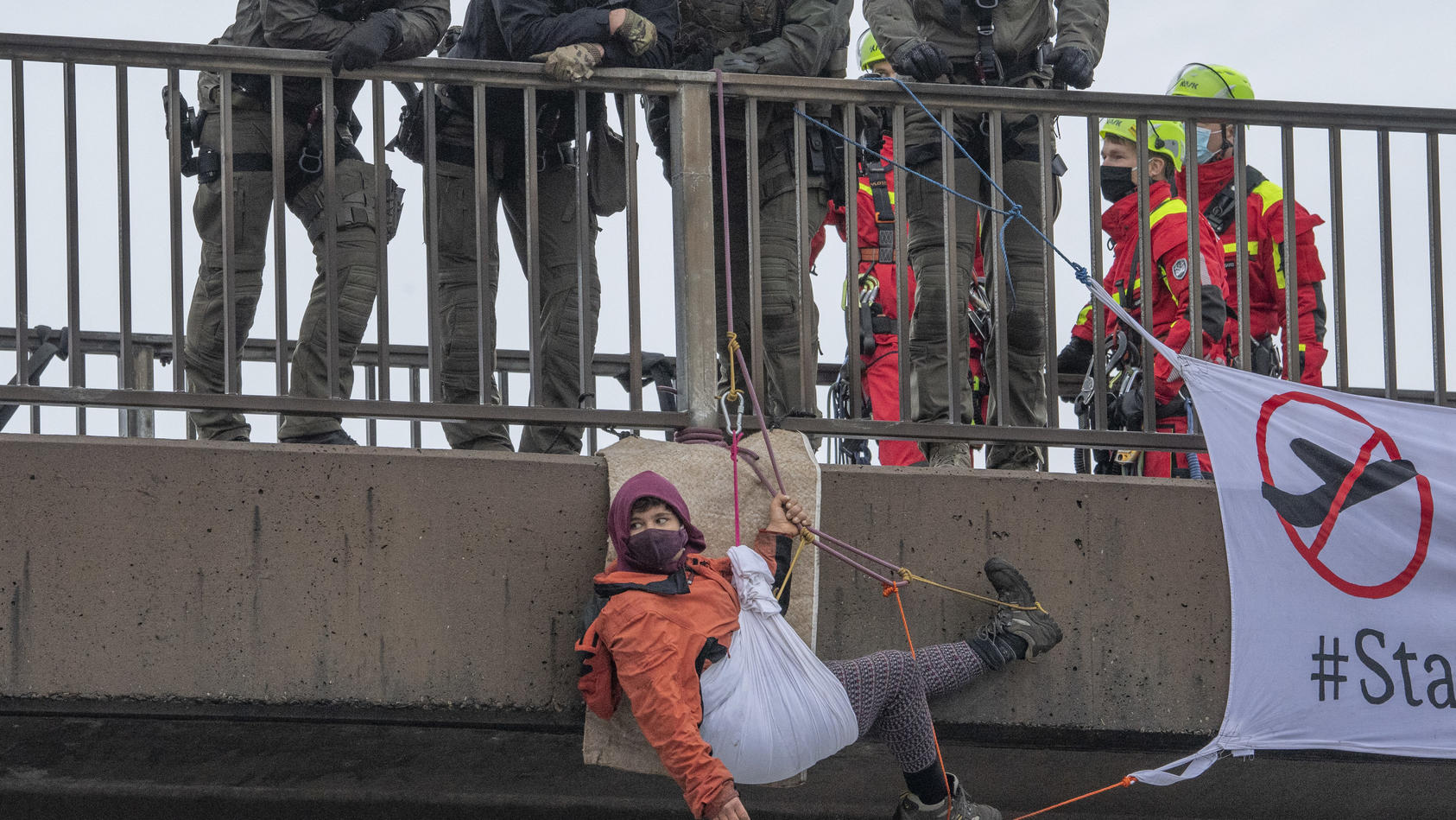 26.10.2020, Hessen, Zeppelinheim: Eine Aktivistin hängt an einer Brücke über die Autobahn 5 am Frankfurter Flughafen. Polizisten vom SEK und Feuerwehrleute sind dabei im Einsatz. Zeitgleich hatten sich am Montagmorgen mehrere Gruppen von Umweltschütz