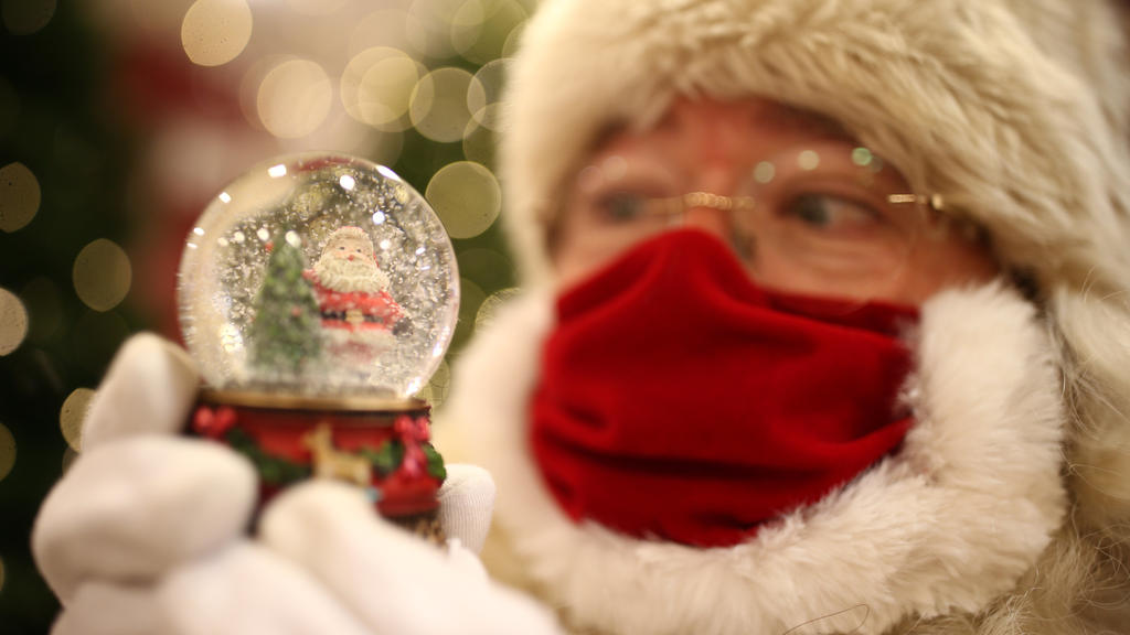 12.10.2020, Großbritannien, London: Ein als Weihnachtsmann verkleideter Mann hält in einer Filiale des Kaufhauskette Selfridges mit Mund-Nasen-Schutz eine Schneekugel in den Händen. Das diesjährige Thema wurde unter dem Motto «Once Upon A Christmas»