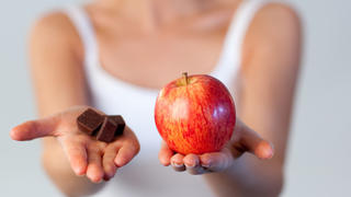 Close-up of an young beautiful woman showing chocolate and an apple with focus on apple