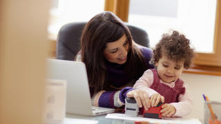 businesswoman working with laptop computer at home and playing with her baby girl. Horizontal shape, front view, waist up