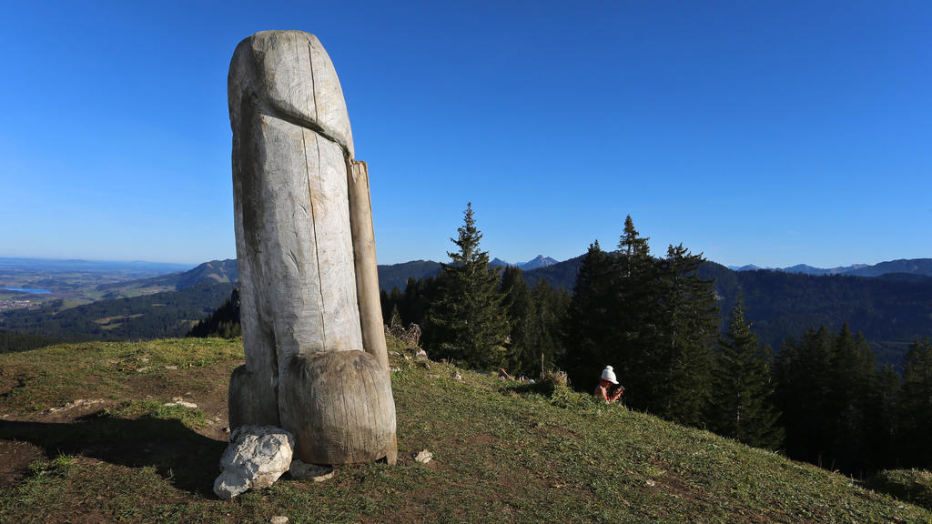 14.11.2020, Bayern, Rettenberg: Eine Wanderin rastet hinter der zwei Meter hohen Penis-Skulptur aus Holz auf dem Grat des Grünten. Seit vier Jahren steht das ungewöhnliche «Kulturdenkmal» auf dem Berg. (zu dpa «Kulturdenkmal»: Holzpenis auf Allgäuer