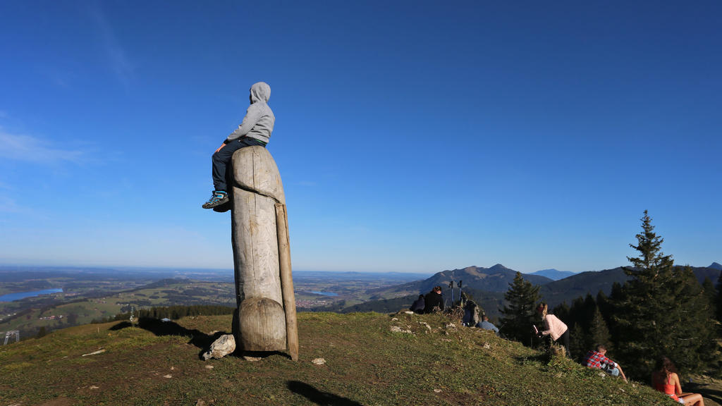 14.11.2020, Bayern, Rettenberg: Ein Junge sitzt auf der zwei Meter hohen Penis-Skulptur aus Holz auf dem Grat des Grünten. Seit vier Jahren steht das ungewöhnliche «Kulturdenkmal» auf dem Berg. (zu dpa «Kulturdenkmal»: Holzpenis auf Allgäuer Berg ste