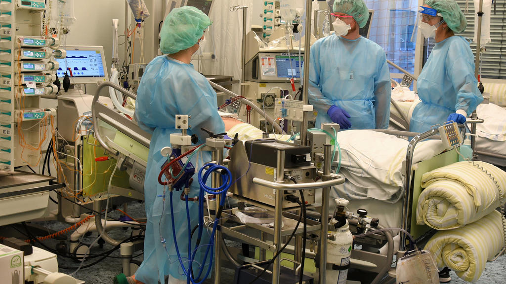 17.11.2020, Sachsen, Leipzig: Auf der Covid-Station, einem Bereich der Operativen Intensivstation vom Universitätsklinikum Leipzig, stehen ein Arzt (2.v.r.) und zwei Schwestern an Betten von Patienten. Auf der Operativen Intensivstation stehen mit ei