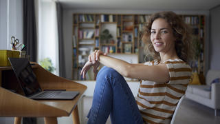  Woman smiling while sitting by desk on chair at home model released Symbolfoto property released RBF08032