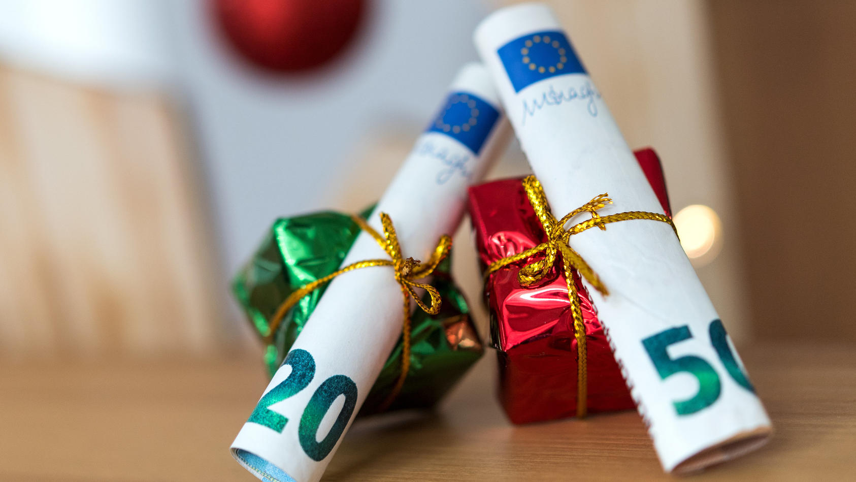 ILLUSTRATION - 04.12.2018, Sachsen, Dresden: ARCHIV - Als Geschenk verpackte 20 und 50 Euro Banknoten liegen auf einem Tisch.  Weihnachten steht vor der Tür und damit auch der Stress, die richtigen Geschenke zu finden. Noch beliebter als liebevoll au