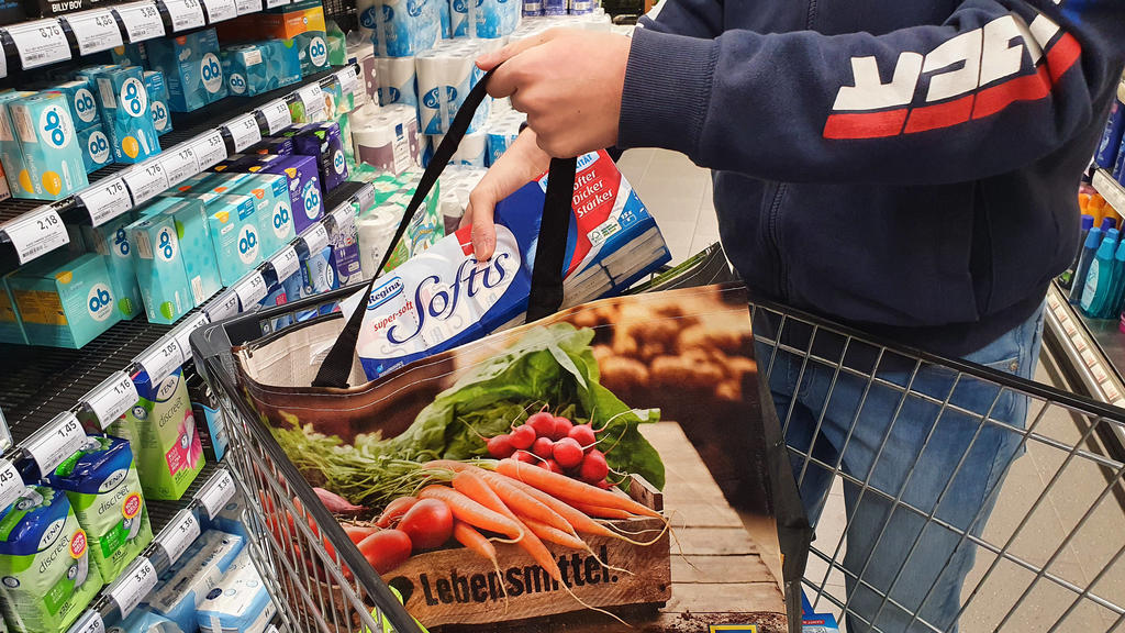 In einer Aldi-Filiale sieht man einen Mann einkaufen. In seinem Einkaufswagen liegen seine Einkäufe, unter anderem unverpacktes Gemüse.