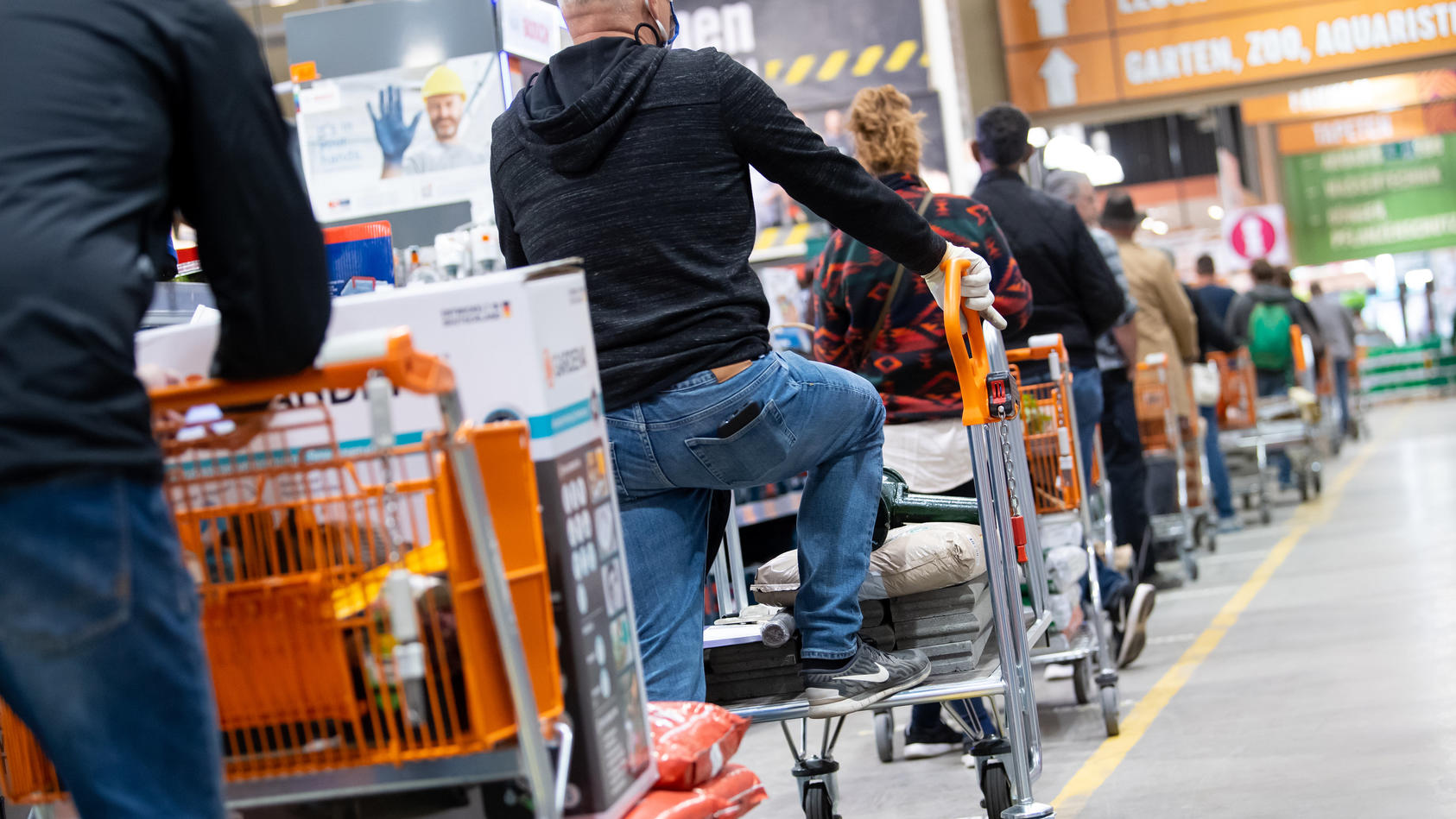 ARCHIV - 20.04.2020, Bayern, München: Kunden stehen mit Einkaufswagen in einem Hornbach-Baumarkt in einer Schlange vor den Kassen an. Die Corona-Krise beschert den Bau- und Gartenfachmärkten in Deutschland einen anhaltenden Nachfrageboom. (zu dpa "Ba
