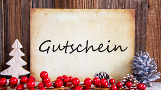 Papier mit Aufschrift Gutschein vor Holzwand und mit Weihnachtsdeko