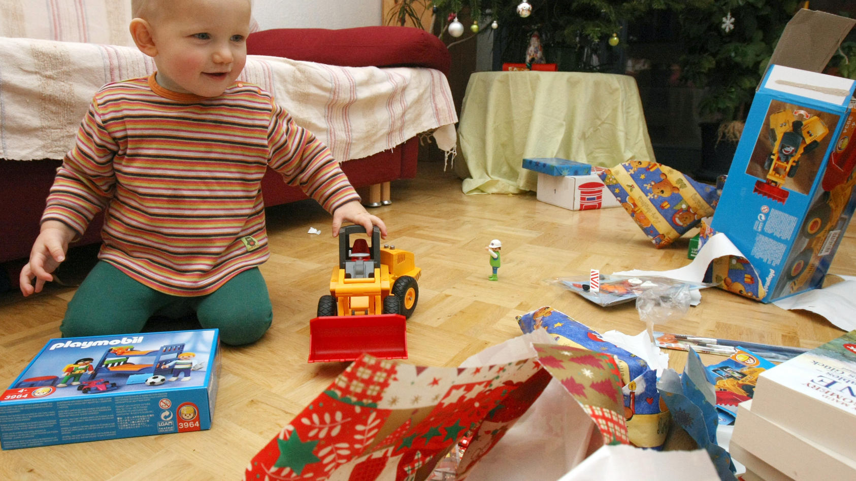ARCHIV  - Der kleine Janne freut sich an Weihnachten beim Auspacken seiner Geschenke. Im Hintergrund steht der festlich geschmückte Weihnachtsbaum. Aufnahme vom 24.12.2007. Plätzchen, Weihnachtslieder, ein festlich geschmückter Tannenbaum: Am Heilige