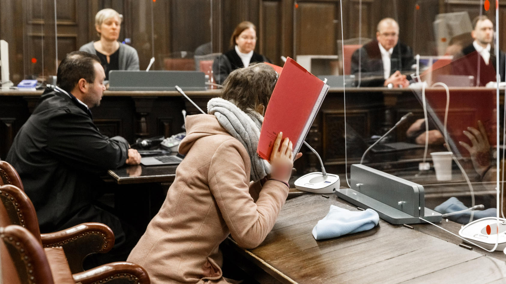 23.12.2020, Hamburg: Die 37-jährige Angeklagte (vorne) sitzt im Gerichtssaal neben ihrem Anwalt und verbirgt ihr Gesicht hinter einem Aktendeckel im Prozess wegen Mordes an ihrem 80-jährigem Ex-Freund. Der Angeklagten wird vorgeworfen, im April ihren