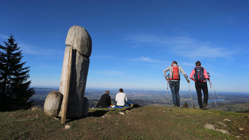 14.11.2020, Bayern, Rettenberg: Wanderer genießen neben der zwei Meter hohen Penis-Skulptur aus Holz auf dem Grat des Grünten den Ausblick. Seit vier Jahren steht das ungewöhnliche «Kulturdenkmal» auf dem Berg. (zu dpa «Kulturdenkmal»: Holzpenis auf