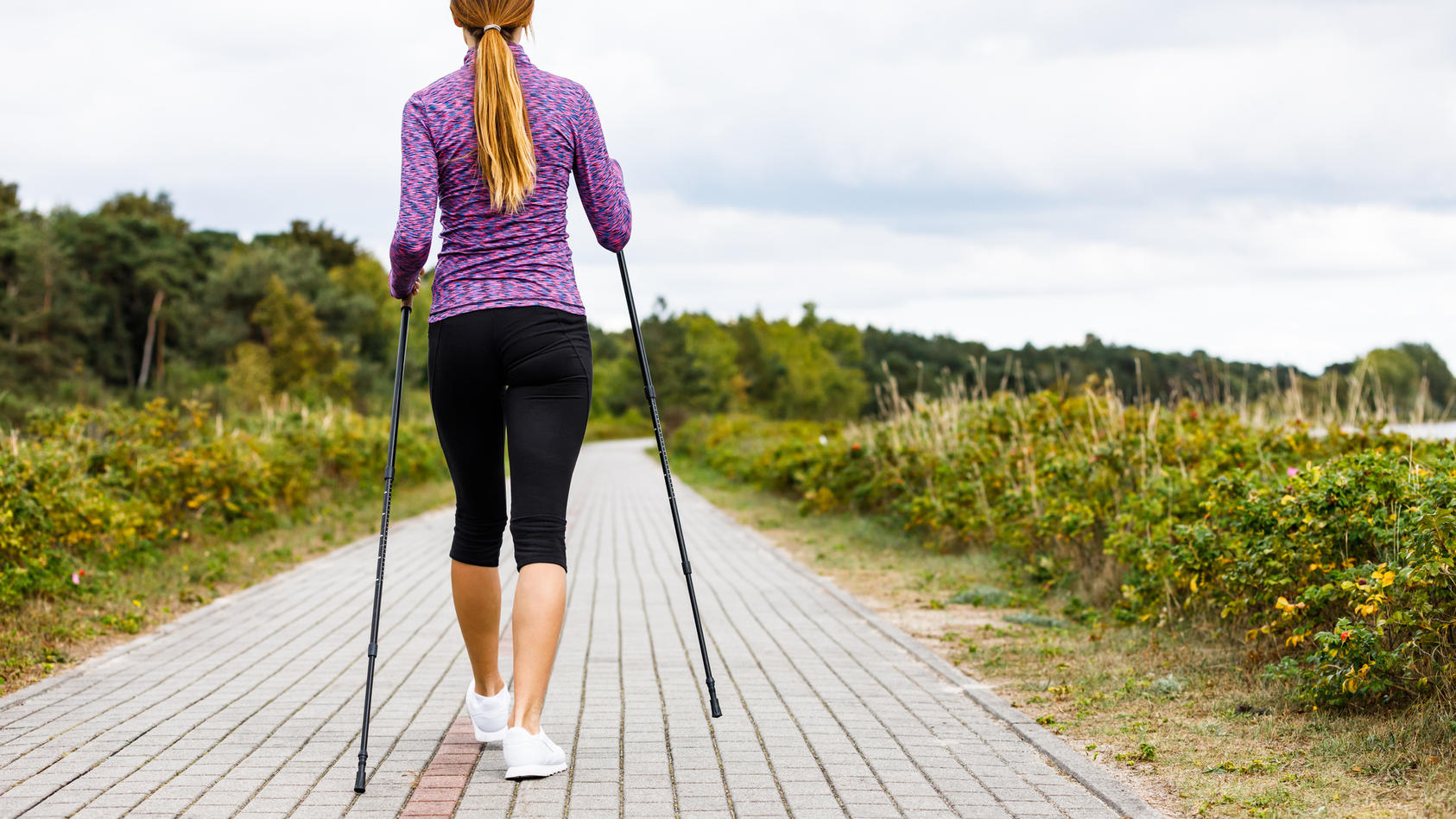 Junge Frau in Sportkleidung beim Nordic Walking mit Stöcken
