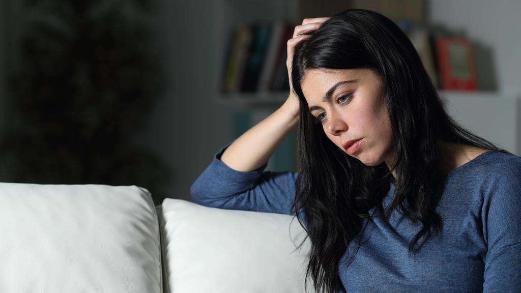 Junge Frau grübelt auf dem Sofa: Depressionen können schleichend beginnen