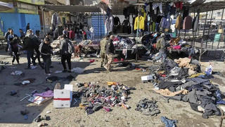 21.01.2021, Irak, Bagdad: Menschen und Sicherheitskräfte gehen in der irakischen Hauptstadt am Ort eines tödlichen Anschlags, einem Markt, auf dem gebrauchte Kleidung verkauft wurde, an auf dem Boden verstreuten Kleidung und Schuhen vorbei. Bei zwei Selbstmordanschlägen in Bagdad sind am Donnerstag mindestens 21 Menschen getötet und 50 weitere verletzt worden. Foto: Hadi Mizban/AP/dpa +++ dpa-Bildfunk +++