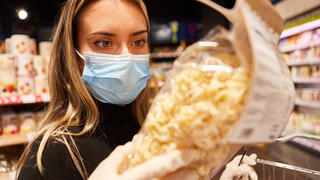 Frau als Kundin mit Maske wegen Covid-19 Pandemie beim Pasta Kauf im Supermarkt