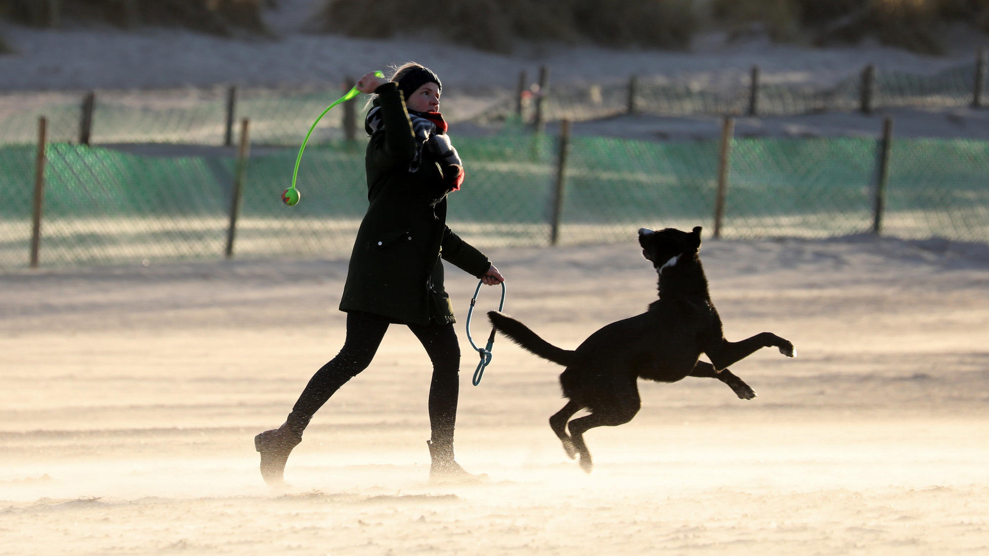 21.01.2021, Mecklenburg-Vorpommern, Warnemünde: Eine Frau ist mit ihrem Hund am Ostseestrand unterwegs, im schrägen Licht der aufgehenden Sonne leuchtet der Sand hell. Nach dem tagelangen Schmuddelwetter mit Regen und Schnee ist sie ein seltener Gast