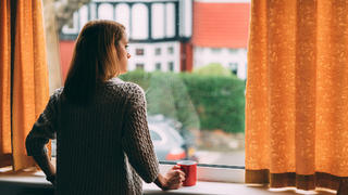 Frau steht am Fenster mit Tasse Kaffee in der Hand