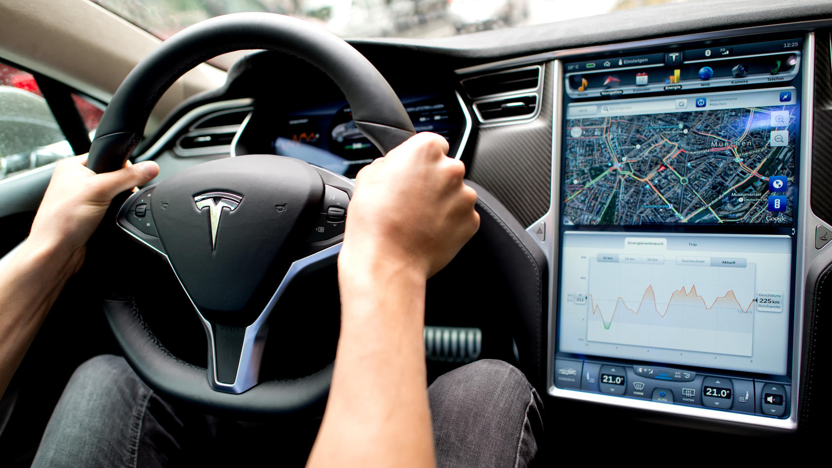 ARCHIV - 17.08.2015, Bayern, München: Ein Mann sitzt in einem Tesla Model S am Lenkrad, neben ihm ein großer Monitor im Armaturenbrett.   (zu dpa "Behörde prüft Fehlfunktion von Tesla-Bildschirm") Foto: picture alliance / dpa +++ dpa-Bildfunk +++