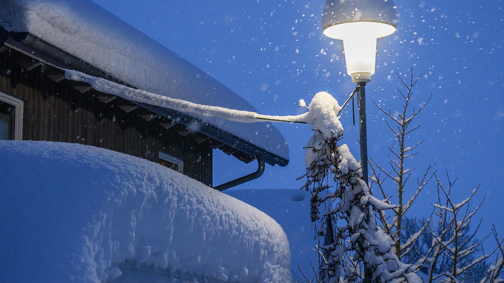 Eine Strassenlaterne leuchtet an einem Wintermorgen bei Schneefall zur blauen Stunde in Leutkirch in Baden Württemberg