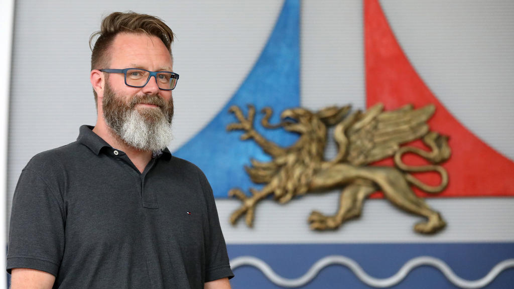 21.08.2020, Mecklenburg-Vorpommern, Rostock: Claus Ruhe Madsen, Oberbürgermeister, steht im Bürgerschaftssaal neben dem Stadtlogo. Der Däne wurde vor einem Jahr Oberbürgermeister der größten Stadt Mecklenburg-Vorpommerns. Foto: Bernd Wüstneck/dpa-Zen