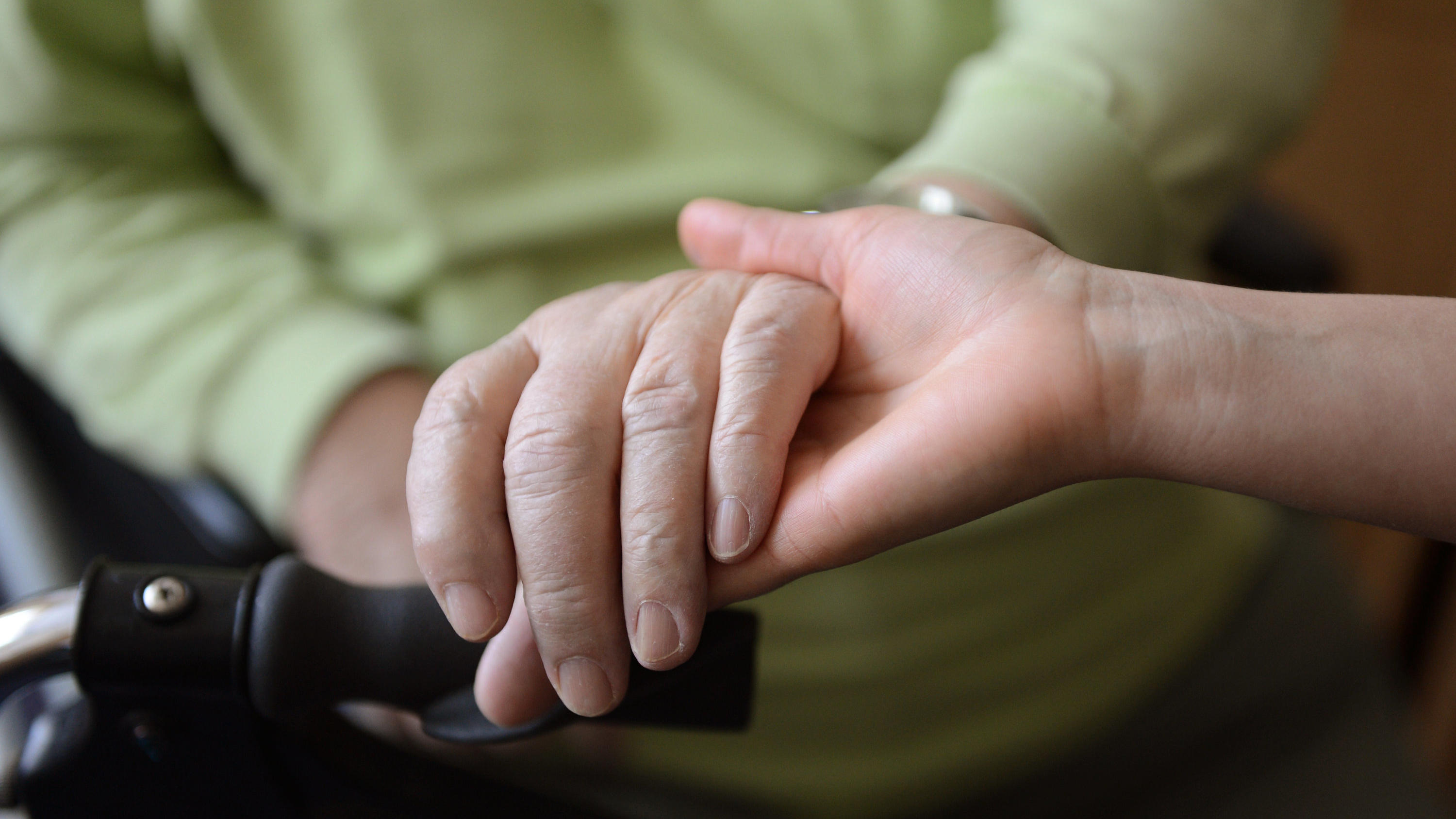 Hand einer Pflegerin hält die Hand einer Heimbewohnerin