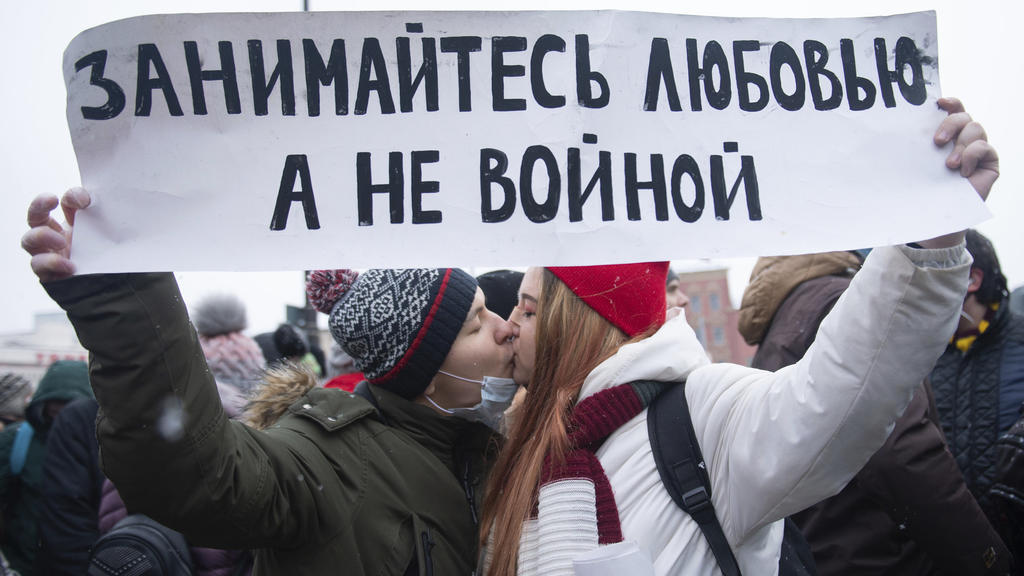 31.01.2021, Russland, Moscow: Junge Demonstranten küssen sich bei einem Protest gegen die Inhaftierung des Kremlkritikers Nawalny und halten ein Transparent, auf dem steht: "Make love, not war". Tausende von Menschen gingen in ganz Russland auf die S