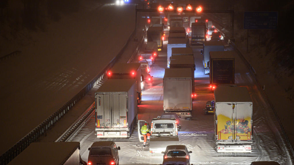 08.02.2021, Sachsen, Dresden: Autos und Lastwagen stehen am frühen Morgen bei Schneefall auf der verschneiten Autobahn 4 bei Dresden im Stau, während ein Mann neben seinem Auto steht. Foto: Robert Michael/dpa-Zentralbild/dpa +++ dpa-Bildfunk +++