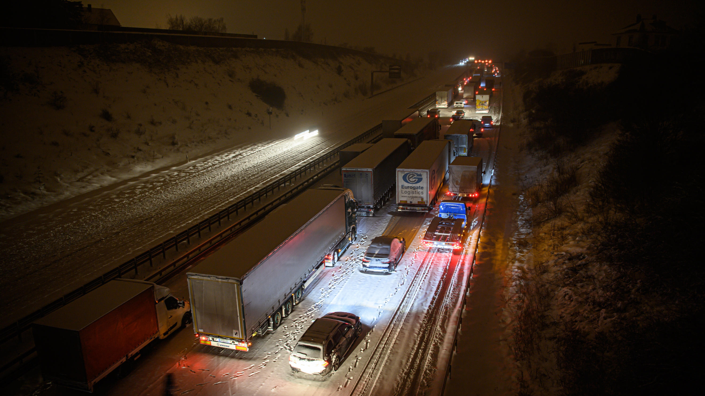 08.02.2021, Sachsen, Dresden: Autos und Lastwagen stehen am frühen Morgen bei Schneefall auf der verschneiten Autobahn 4 bei Dresden im Stau, während ein Mann neben seinem Auto steht. Foto: Robert Michael/dpa-Zentralbild/dpa +++ dpa-Bildfunk +++