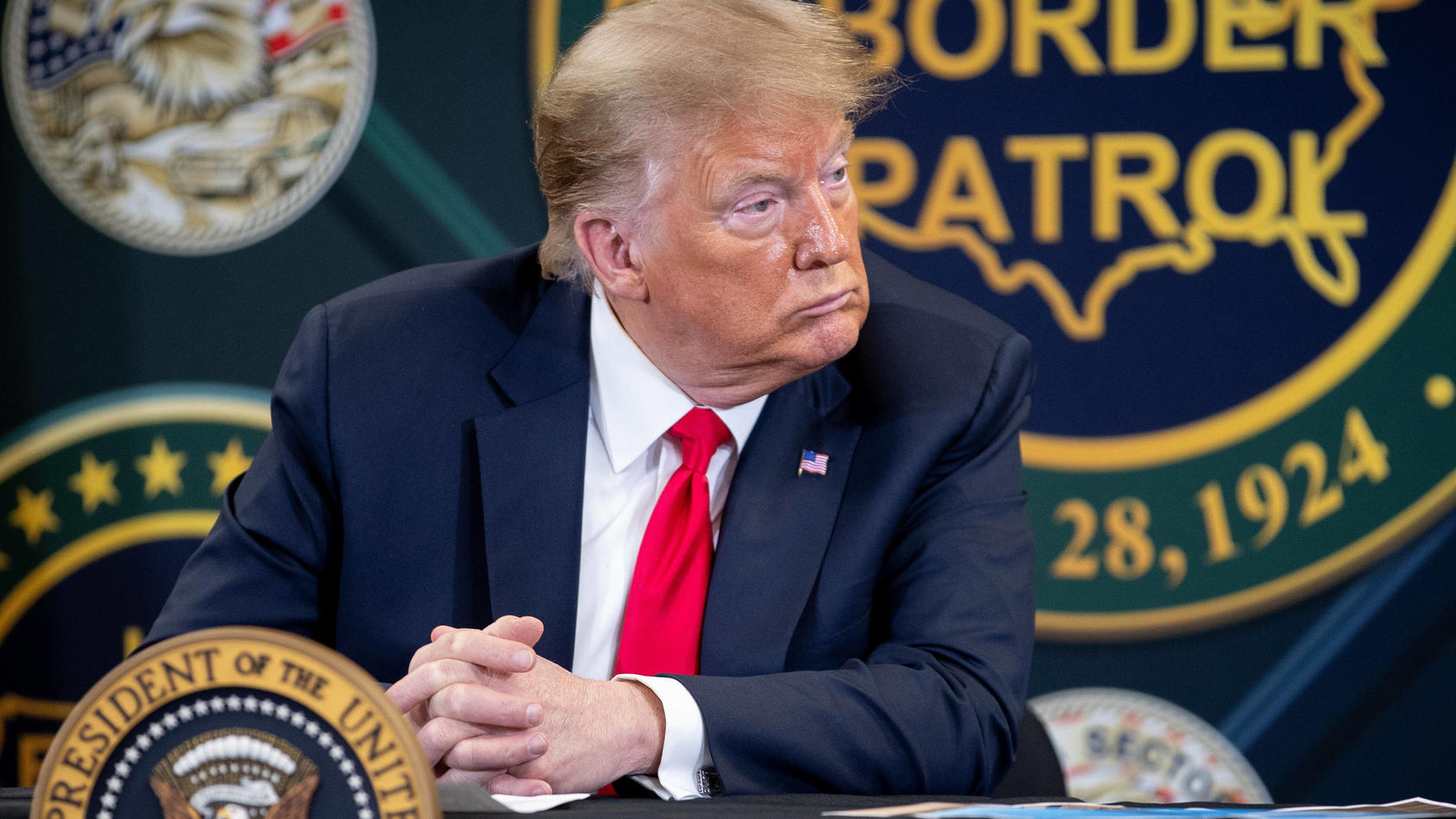  Der ehemalige US-Präsident Donald Trump sitzt einem Pult und schaut nachdenklich in die Ferne.
